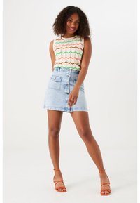 Mouwloos crèmekleurig topje met groene, oranje en bruine golfpatronen; gecombineerd met een lichtblauwe denim A-lijn mini-rok met voorzakken.