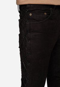 Schwarze Denim-Jeans mit Schnürdetails an der Seite, ausgestattet mit Ösen und schwarzen Schnürsenkeln, klassischer Fünf-Taschen-Design und einer glatten Textur.
