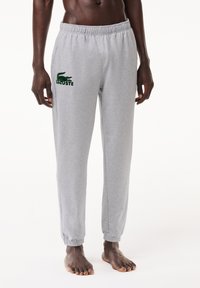 Grå bomulls joggebukser med elastisk liv, detaljerte ankler og en grønn Lacoste-logo på venstre lår. Glatt tekstur, avslappet passform.