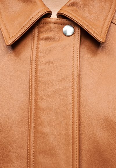 Καφέ δερμάτινο γιακάς μπουφάν με ορατή ραφή και ένα ασημένιο κουμπί τύπου σκραπ στη μέση εμπρός.