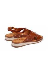 Sandalias de cuero marrón con tiras cruzadas, que presentan acentos plateados en los agujeros y una suela de plataforma de color claro. Hebilla ajustable en el talón.
