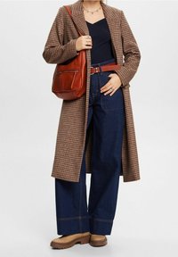 Ruskea ruudullinen pitkä takki tummansinisen paidan päällä, yhdistetty leveälahkeisiin tummansinisiin farkkuihin, punaisella vyöllä ja ruskealla nahkalaukulla. Ruskeat paksupohjaiset saappaat.