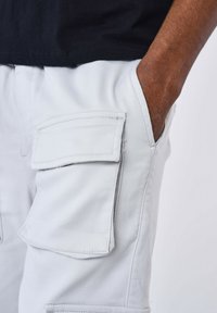 Pantalones cargo de color gris claro con bolsillos laterales, hechos de una tela suave. Presentan una cintura ajustada y detalles de costura limpia.