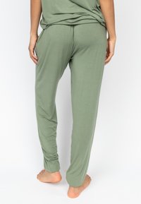 Olijf groene loungebroeken met een zachte textuur, taps toelopende pijpen en een elastische tailleband, gezien van de achterkant met handen in de zakken.