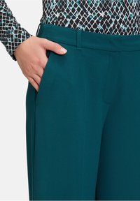 Teal op maat gemaakte broek met een gladde textuur, rechte snit, zijzakken en een strakke tailleband, gecombineerd met een geblokte top met lange mouwen.