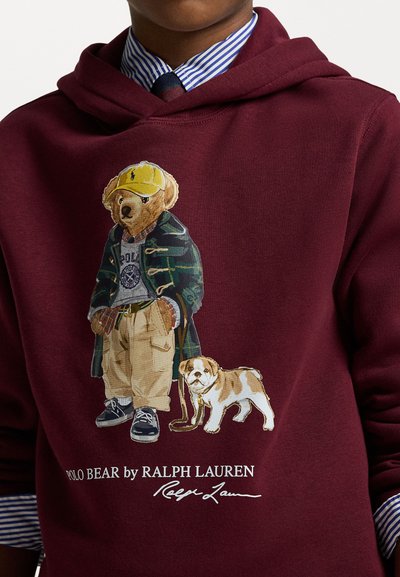 Bordo kapuca majica z grafiko medveda v sproščenem oblačilu, ki nosi karo srajco, karo hlače in psa ob sebi, z znamko "POLO MEDVED".
