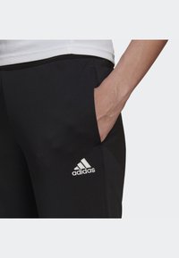 Black jogger pants with side pockets, featuring white Adidas logo embroidery on the left thigh and a smooth, textured fabric.