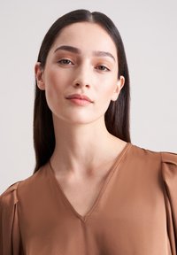 Braune V-Ausschnitt-Bluse mit weicher, seidiger Textur und dezenten Falten an den Schultern. Der Stoff fällt geschmeidig und präsentiert ein minimalistisches Design.