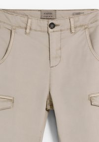 Pantalones beige ajustados hechos de un tejido ligero, con cierre de botón en la parte delantera, bolsillos laterales y bolsillos estilo cargo en los muslos.