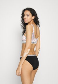 Svarte dametruser har en logo i midjen. Bralette-en har et flerfarget mønster i rødt og rosa med en logo under bandet.