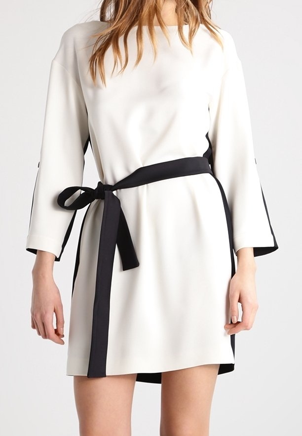 Robe blanche avec des manches trois-quarts et une ceinture noire. Coupe droite et accents latéraux noirs. Texture de tissu lisse.