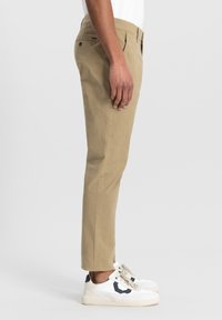 Chino slim-fit bej cu buzunare laterale, bucle pentru curea și o textură netedă, asortați cu adidași albi cu un accent bleumarin.