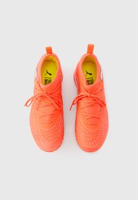 Lyse koralfarvede atletikskøjter med en tekstureret overdel, cirkulære perforeringer og et mønster. Har en tæt pasform og en trækskinne ved hælen.
