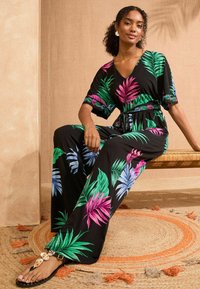Čierny overal s farebnými tropickými vzormi listov v zelených, ružových a modrých odtieňoch, so zúženým pásom a krátkymi rukávmi.