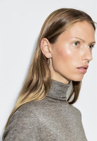 Silver hoop earrings worn with a gray turtleneck sweater. Smooth texture, cylindrical shape with a slight curve. Minimalistic design.