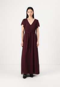 Burgundy maxi dress with short ruffled sleeves, deep V-neck, and an elastic waistband. Smooth, lightweight fabric falls to the ankles.