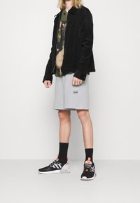 Černá kordurová bunda, maskáčové tričko, světle šedé šortky, černo-bílé tenisky s akcenty a černé ponožky. Jednoduchý, neformální outfit.