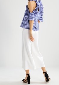 Blå och vit rutig topp med volangärmar och öppen rygg, i kombination med vita vida byxor och svarta högklackade sandaler.