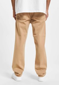 Pantalones beige de algodón con un corte relajado, que cuentan con dos bolsillos traseros y una textura suave, combinados con zapatillas blancas.