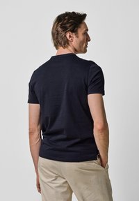 Marinblå t-shirt med kort ärm i bomull, designad med en klassisk rund halsringning och avslappnad passform; bakview visar en slät textur.