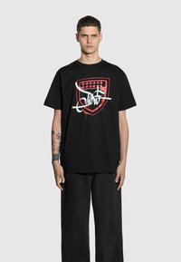 Czarna bawełniana koszulka z dużym czerwono-białym logo graficznym z przodu, o luźnym kroju i krótkich rękawach.