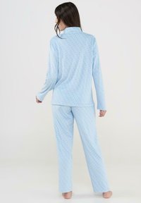 Conjunto de pijama en azul claro hecho de una tela suave, con cuello y un patrón de puntos en azul oscuro y marrón. Corte holgado con mangas largas y pantalones.