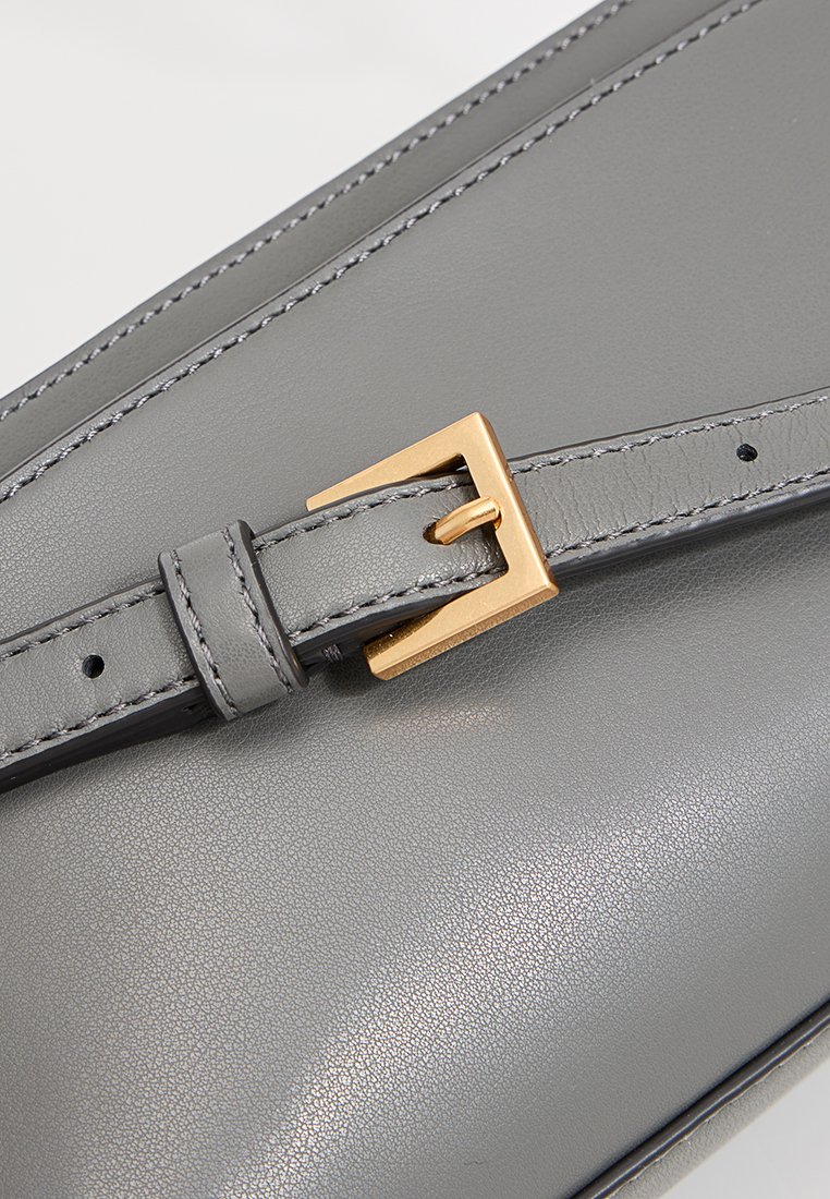 Graue Lederhandtasche mit glatter Textur, goldfarbener Schnallendetail und kontrastierenden Nähten am Riemen.