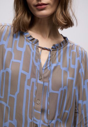 Hnědá halenka s modrým geometrickým vzorem, s řaseným výstřihem, zapínáním na knoflíky a otvorem ve tvaru klíčové dírky vpředu. Měkká textura látky.