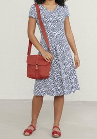 Modrá a bílá vzorovaná šaty s krátkým rukávem, doplněné červenou plátěnou taškou přes rameno a červenými sandály se řemínky.