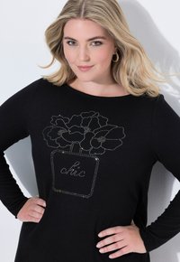 Schwarzes Langarmoberteil mit einem mit Strass verzierten Blumenkrug-Design und dem Wort "Chic" in der Mitte. Weicher Stoff, figurbetonte Passform.