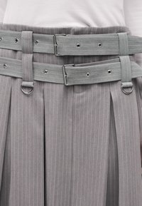 Κοντινή λήψη από γκρι φούστα με ρίγες, με δύο ταιριαστά υφασμάτινα ζώνες στερεωμένες και ραμμένες θηλιές ζώνης με μεταλλικούς D-δακτυλίους.