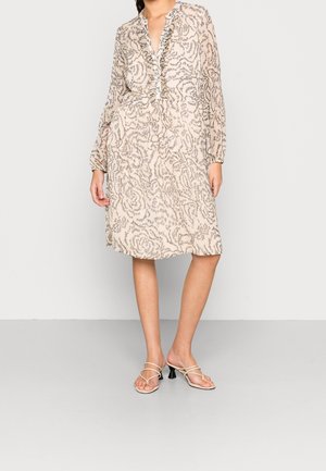 Hellbeiges Kleid mit floralem Muster, gerafftem Ausschnitt, langen Ärmeln und tailliertem Bund. Kombiniert mit rückenfreien Absatzsandalen.