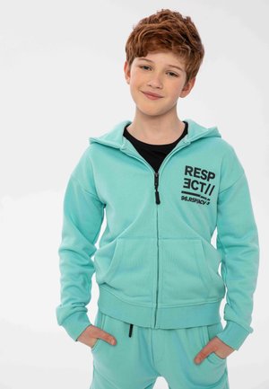Felpa con zip di colore azzurro chiaro, dotata di tasche frontali e stampa nera con la scritta "RESPECT//96.RSPICY." Abbinata a pantaloni della tuta coordinati, dal design aderente.