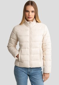 Lys beige pufferjakke med høj krave, quiltet mønster, to sidelommer og lynlås foran. Blødt, blankt materiale.