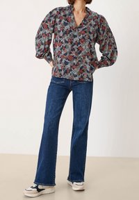 Blusa con motivo floreale e maniche a sbuffo nei colori blu navy, rosso e verde; abbinata a jeans a zampa d'elefante blu scuro e sneakers bianche e blu navy.