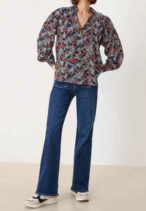 Blusa con motivo floreale e maniche a sbuffo nei colori blu navy, rosso e verde; abbinata a jeans a zampa d'elefante blu scuro e sneakers bianche e blu navy.