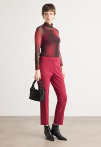 Langsleeve doorschijnende top in een verloop van rood naar zwart, gecombineerd met op maat gemaakte rode broeken. Model houdt een kleine zwarte handtas vast; draagt zwarte enkellaarsjes.