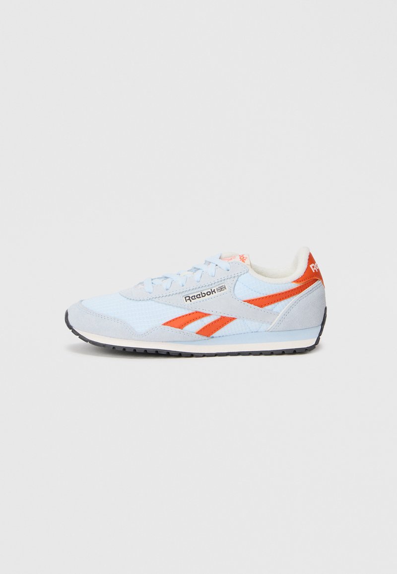 Gaiši zili un oranži Reebok sporta apavi ar zamšādas pārklājumiem, logotipu un melnu zoli uz vienkārša baltā fona, sānu skats.
