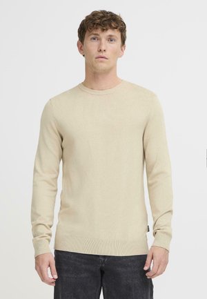 Beige knitted sweater with long sleeves, round neckline, ribbed cuffs and hem, featuring a subtle texture and a small label at the waist.