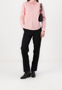 Rood en wit gestreept shirt met een gespspuntige kraag, zwarte op maat gemaakte broek en zwarte hielboots. Inclusief een kleine zwarte handtas.