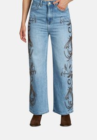Jeans de mezclilla anchos de color azul claro con intrincados bordados en forma de flores de color marrón oscuro en los laterales, con una cintura alta y un diseño clásico de cinco bolsillos.