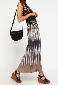 Robe longue en tissu côtelé, présentant un dégradé noir et beige avec des rayures verticales. Associée à des sandales compensées noires et un sac bandoulière noir.