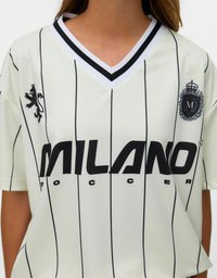 Vit fotbollströja med svarta vertikala ränder, med en svart lejonlogotyp, ett runt emblem och "MILANO" tryckt framträdande i svart.