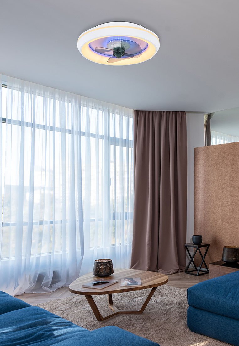 Stropní ventilátor s kulatým bílým rámem, transparentními lopatkami a LED světly vytvářejícími modrou záři, instalovaný v moderní místnosti s velkými okny.