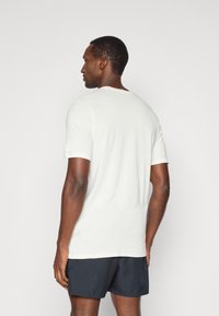 Λευκό T-shirt κοντομάνικο με στρογγυλή λαιμόκοψη και μπλε ραφές, συνδυασμένο με σκούρα σορτς. Μαλακό ύφασμα με λεία υφή.