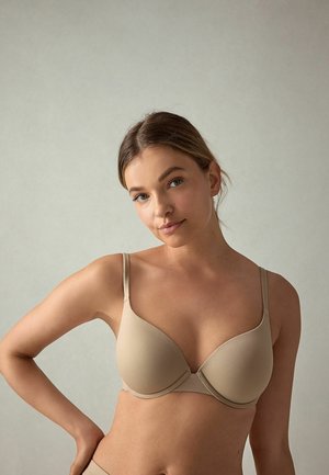 Beige gevoerde beha met verstelbare bandjes, met een gladde textuur en naaddetails, ontworpen voor een ondersteunende pasvorm.