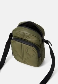 Grøn, kviltet nylon skuldertaske med sort lynlås og justerbar rem. Har et geometrisk mønster og en blød tekstur.