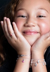 Silberne Armbänder an beiden Handgelenken zeigen Charms wie einen Marienkäfer, Herzen und Friedenssymbole. Ein schlichter silberner Ring ergänzt die Accessoires.