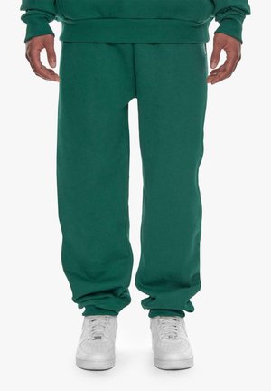 Grüne Jogginghose aus weichem Material, mit legere Passform, Rippbündchen und seitlichen Taschen. Kombiniert mit weißen Sneakers.