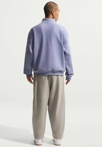 Pullover lavande avec un col montant, une coupe ample et des poignets côtelés, assorti à un pantalon de survêtement gris clair et des baskets blanches.